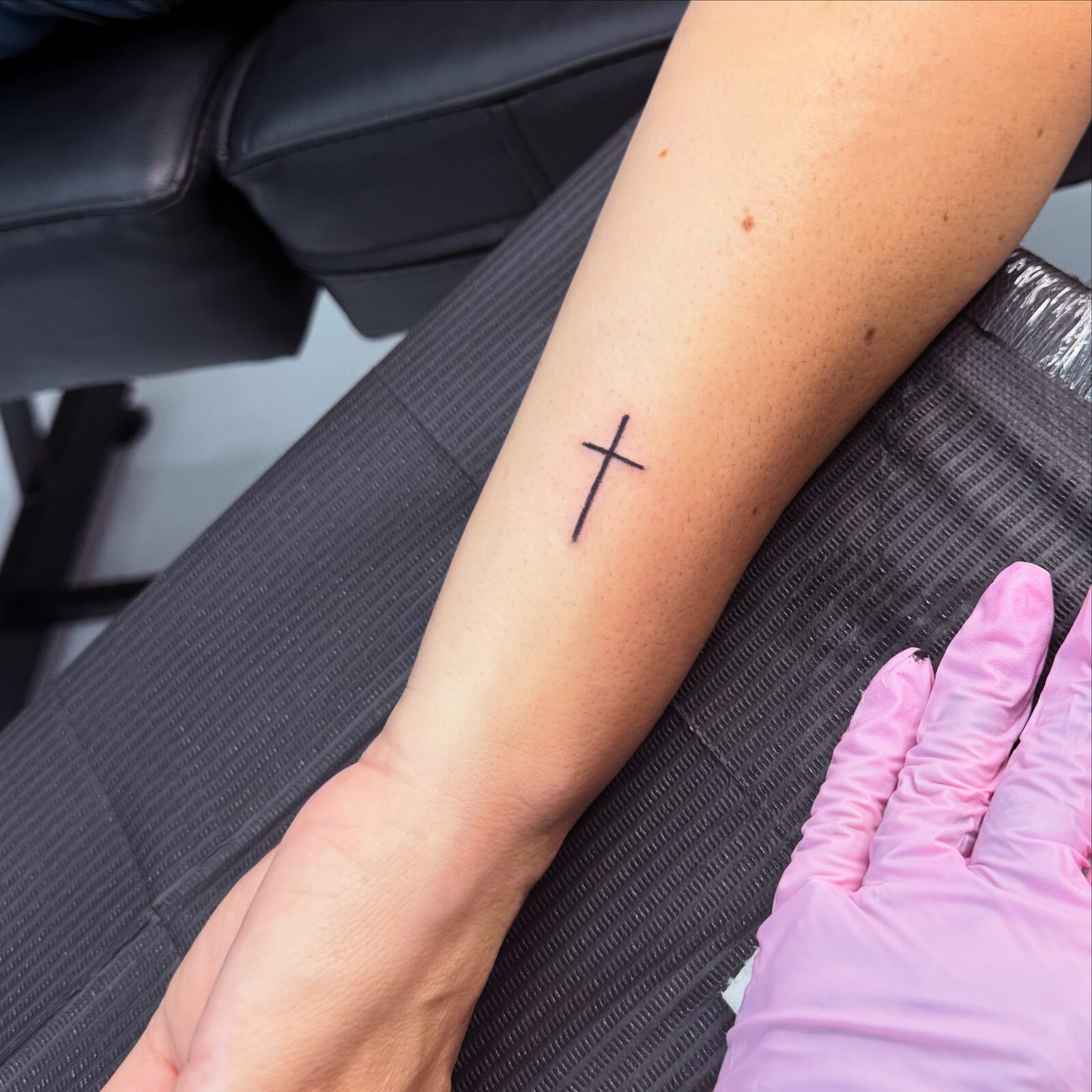 Delicate fine-line cross tattoo on forearm