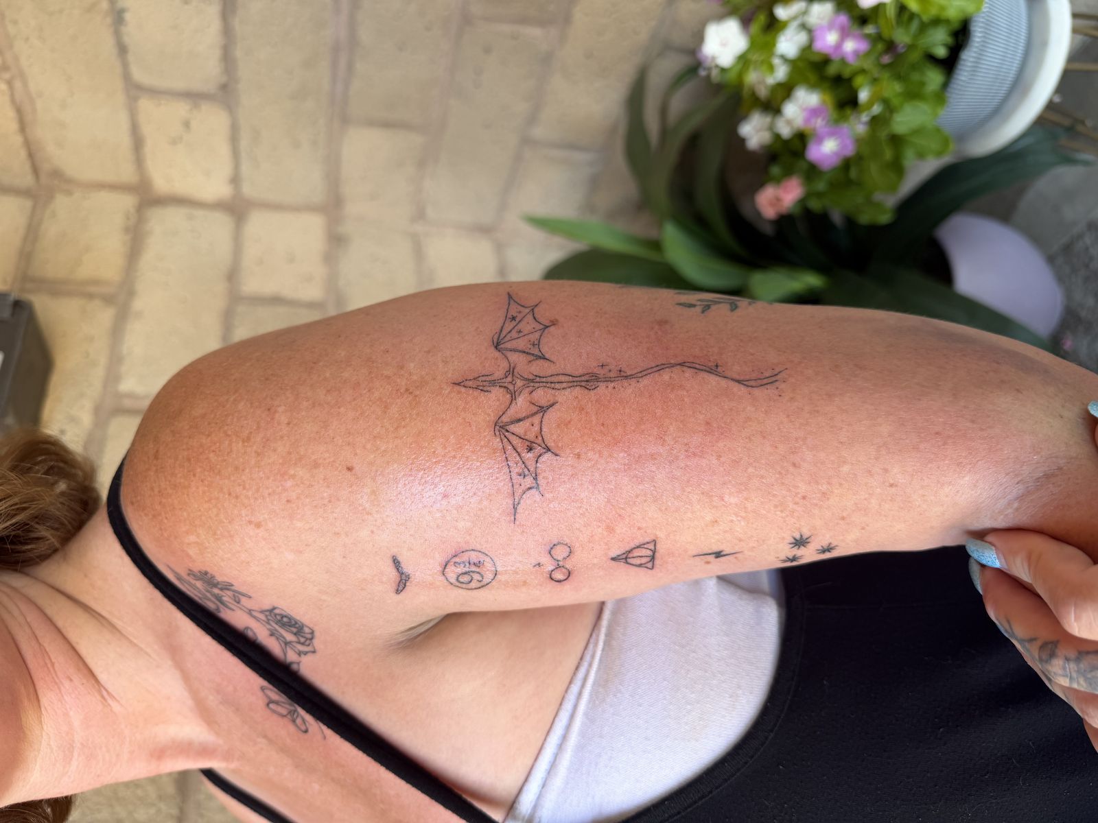 Fine-line dragon tattoo on the upper arm alongside a set of small black-line micro tattoos